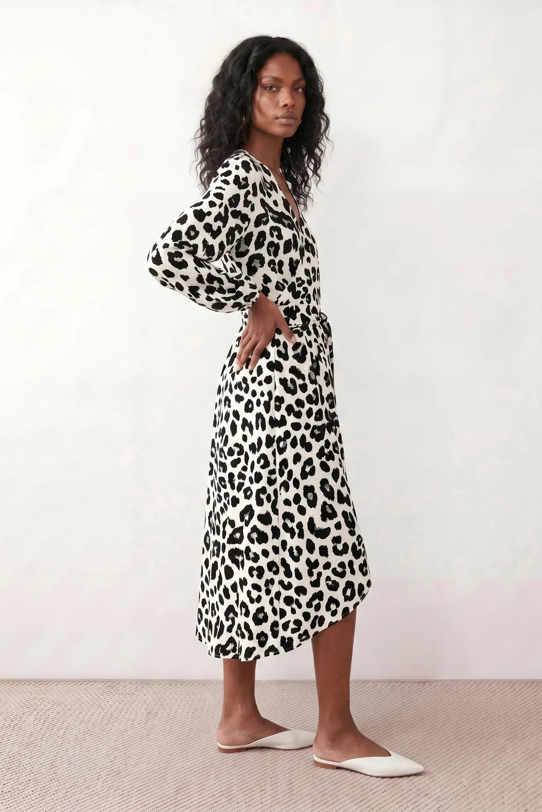 Woman wearing the Rosa Animal Print Wrap Front Midi Dress in a flowing leopard print fabric, featuring a wrap-front V-neckline, adjustable self-tie waist, long sleeves with gathered elasticated cuffs, a high-low midi hem, and a front slit, styled for weddings, cocktail parties, and elegant occasions.