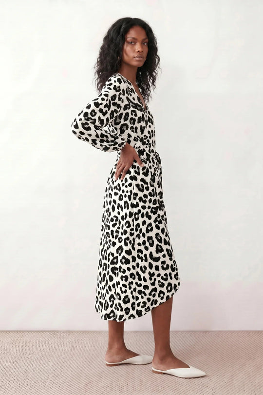 Woman wearing the Rosa Animal Print Wrap Front Midi Dress in a flowing leopard print fabric, featuring a wrap-front V-neckline, adjustable self-tie waist, long sleeves with gathered elasticated cuffs, a high-low midi hem, and a front slit, styled for weddings, cocktail parties, and elegant occasions.