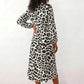 Woman wearing the Rosa Animal Print Wrap Front Midi Dress in a flowing leopard print fabric, featuring a wrap-front V-neckline, adjustable self-tie waist, long sleeves with gathered elasticated cuffs, a high-low midi hem, and a front slit, styled for weddings, cocktail parties, and elegant occasions.