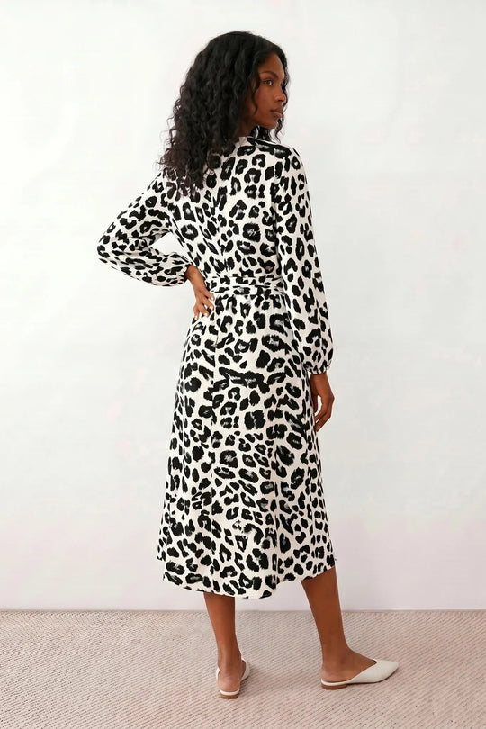 Woman wearing the Rosa Animal Print Wrap Front Midi Dress in a flowing leopard print fabric, featuring a wrap-front V-neckline, adjustable self-tie waist, long sleeves with gathered elasticated cuffs, a high-low midi hem, and a front slit, styled for weddings, cocktail parties, and elegant occasions.