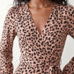 Woman wearing the Rosa Animal Print Wrap Front Midi Dress in a flowing leopard print fabric, featuring a wrap-front V-neckline, adjustable self-tie waist, long sleeves with gathered elasticated cuffs, a high-low midi hem, and a front slit, styled for weddings, cocktail parties, and elegant occasions.