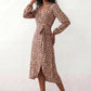 Woman wearing the Rosa Animal Print Wrap Front Midi Dress in a flowing leopard print fabric, featuring a wrap-front V-neckline, adjustable self-tie waist, long sleeves with gathered elasticated cuffs, a high-low midi hem, and a front slit, styled for weddings, cocktail parties, and elegant occasions.
