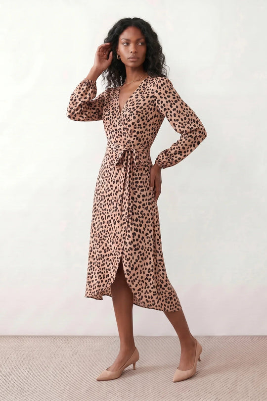 Woman wearing the Rosa Animal Print Wrap Front Midi Dress in a flowing leopard print fabric, featuring a wrap-front V-neckline, adjustable self-tie waist, long sleeves with gathered elasticated cuffs, a high-low midi hem, and a front slit, styled for weddings, cocktail parties, and elegant occasions.
