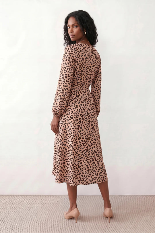 Woman wearing the Rosa Animal Print Wrap Front Midi Dress in a flowing leopard print fabric, featuring a wrap-front V-neckline, adjustable self-tie waist, long sleeves with gathered elasticated cuffs, a high-low midi hem, and a front slit, styled for weddings, cocktail parties, and elegant occasions.