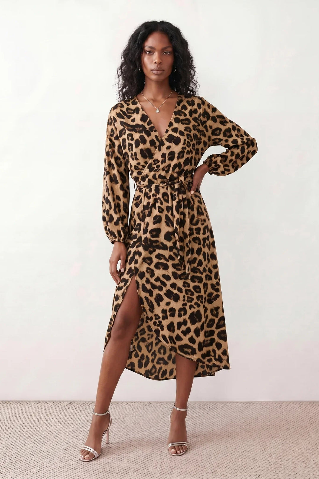 Woman wearing the Rosa Animal Print Wrap Front Midi Dress in a flowing leopard print fabric, featuring a wrap-front V-neckline, adjustable self-tie waist, long sleeves with gathered elasticated cuffs, a high-low midi hem, and a front slit, styled for weddings, cocktail parties, and elegant occasions.