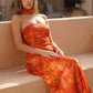 Woman wearing the Diana satin strapless maxi dress featuring a square neckline, scarf-style choker tie, open back with draped detail, and a floor-length fitted silhouette in a smooth satin finish.