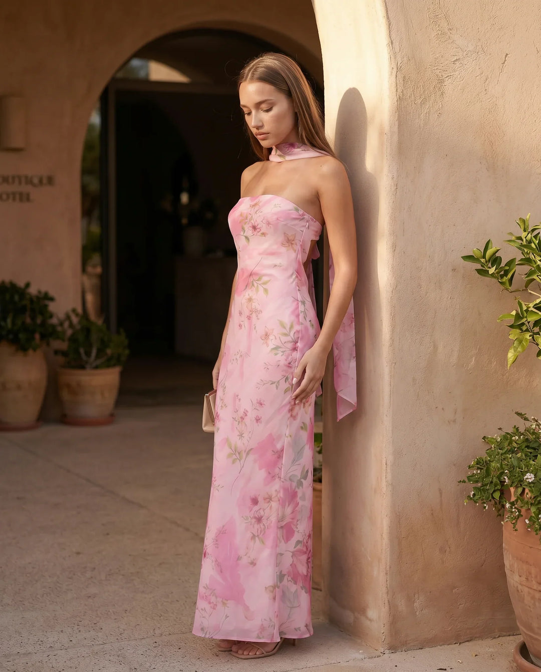 Woman wearing the Diana satin strapless maxi dress featuring a square neckline, scarf-style choker tie, open back with draped detail, and a floor-length fitted silhouette in a smooth satin finish.