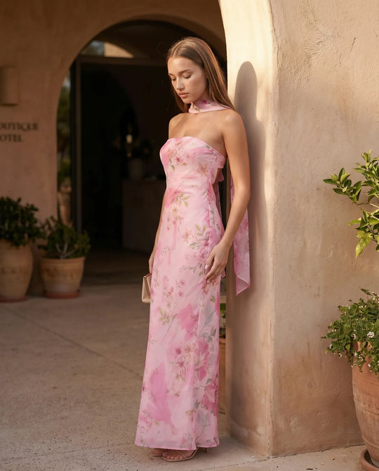 Woman wearing the Diana satin strapless maxi dress featuring a square neckline, scarf-style choker tie, open back with draped detail, and a floor-length fitted silhouette in a smooth satin finish.