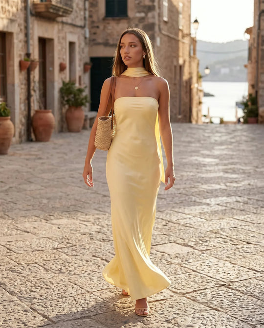 Woman wearing the Diana satin strapless maxi dress featuring a square neckline, scarf-style choker tie, open back with draped detail, and a floor-length fitted silhouette in a smooth satin finish.