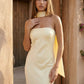 Woman wearing the Diana satin strapless maxi dress featuring a square neckline, scarf-style choker tie, open back with draped detail, and a floor-length fitted silhouette in a smooth satin finish.