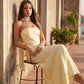 Woman wearing the Diana satin strapless maxi dress featuring a square neckline, scarf-style choker tie, open back with draped detail, and a floor-length fitted silhouette in a smooth satin finish.