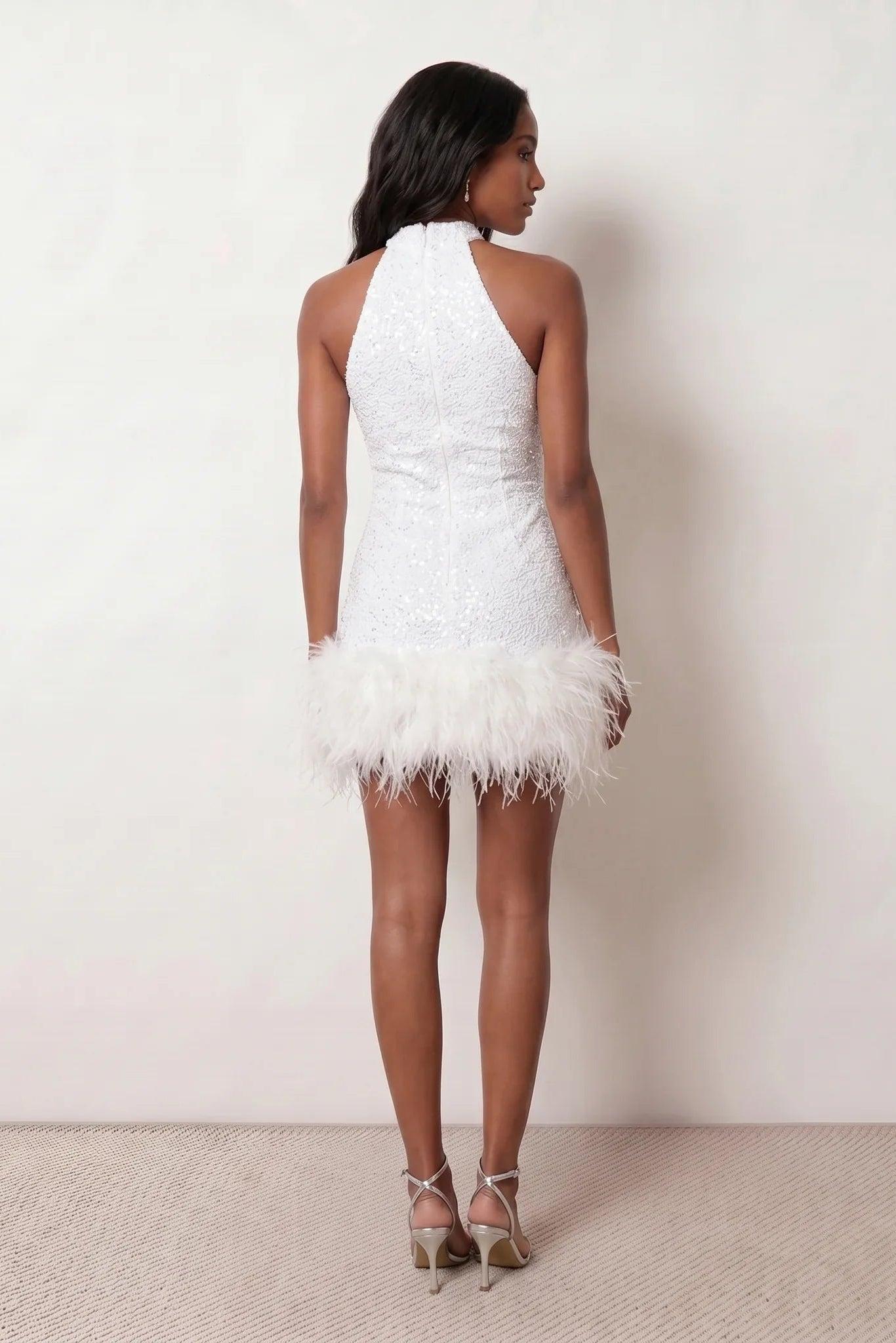Woman wearing the Shanna Sequined Halter Mini Dress featuring all-over shimmering sequins, an elegant halter neckline, striking open back, fitted sheath silhouette, and soft feather-trimmed mini hem, perfect for parties, cocktail events and festive occasions.