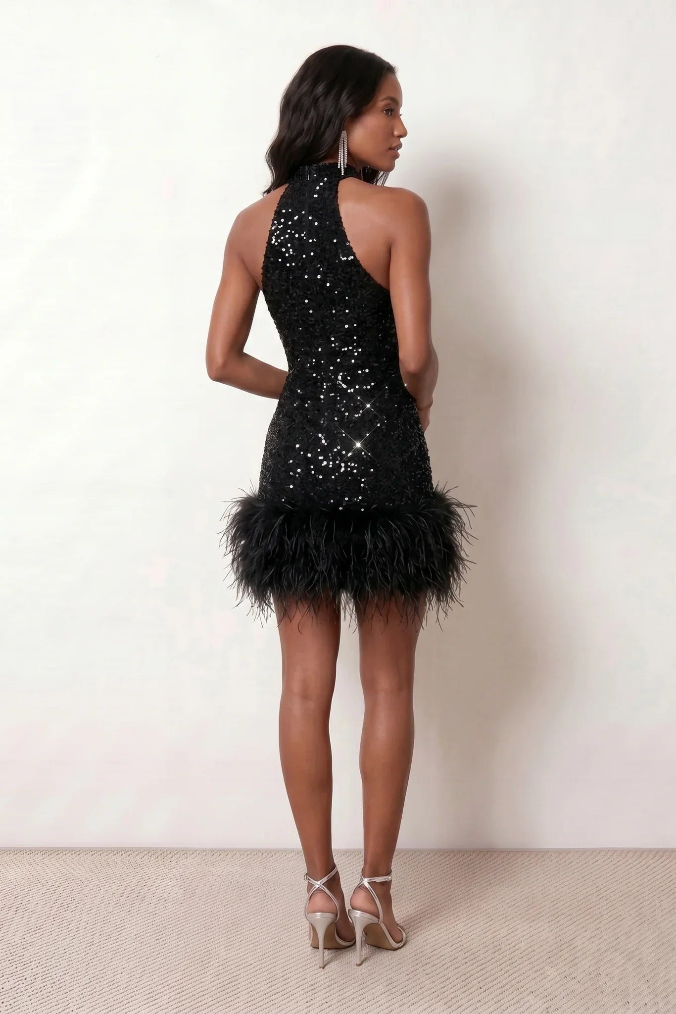Woman wearing the Shanna Sequined Halter Mini Dress featuring all-over shimmering sequins, an elegant halter neckline, striking open back, fitted sheath silhouette, and soft feather-trimmed mini hem, perfect for parties, cocktail events and festive occasions.