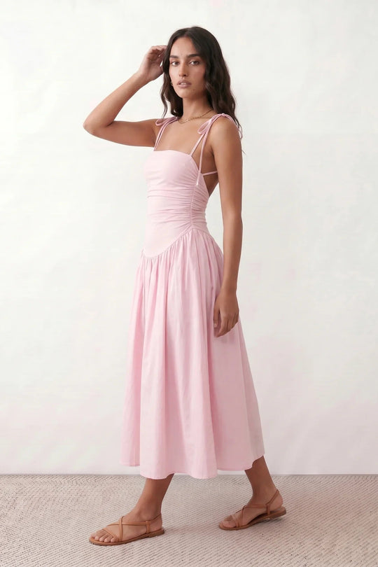 Woman wearing a spaghetti strap low back midi dress with a square neckline, ruched ruffle bodice, adjustable tie shoulder straps, elasticated smocked back, and flowing A-line skirt, styled as an elegant wedding guest and summer occasion dress.