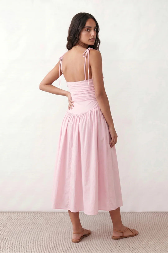 Woman wearing a spaghetti strap low back midi dress with a square neckline, ruched ruffle bodice, adjustable tie shoulder straps, elasticated smocked back, and flowing A-line skirt, styled as an elegant wedding guest and summer occasion dress.