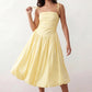 Woman wearing a spaghetti strap low back midi dress with a square neckline, ruched ruffle bodice, adjustable tie shoulder straps, elasticated smocked back, and flowing A-line skirt, styled as an elegant wedding guest and summer occasion dress.