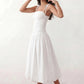Woman wearing a spaghetti strap low back midi dress with a square neckline, ruched ruffle bodice, adjustable tie shoulder straps, elasticated smocked back, and flowing A-line skirt, styled as an elegant wedding guest and summer occasion dress.