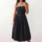 Woman wearing a spaghetti strap low back midi dress with a square neckline, ruched ruffle bodice, adjustable tie shoulder straps, elasticated smocked back, and flowing A-line skirt, styled as an elegant wedding guest and summer occasion dress.