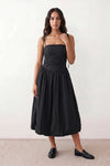 Woman wearing a spaghetti strap low back midi dress with a square neckline, ruched ruffle bodice, adjustable tie shoulder straps, elasticated smocked back, and flowing A-line skirt, styled as an elegant wedding guest and summer occasion dress.