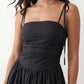 Woman wearing a spaghetti strap low back midi dress with a square neckline, ruched ruffle bodice, adjustable tie shoulder straps, elasticated smocked back, and flowing A-line skirt, styled as an elegant wedding guest and summer occasion dress.
