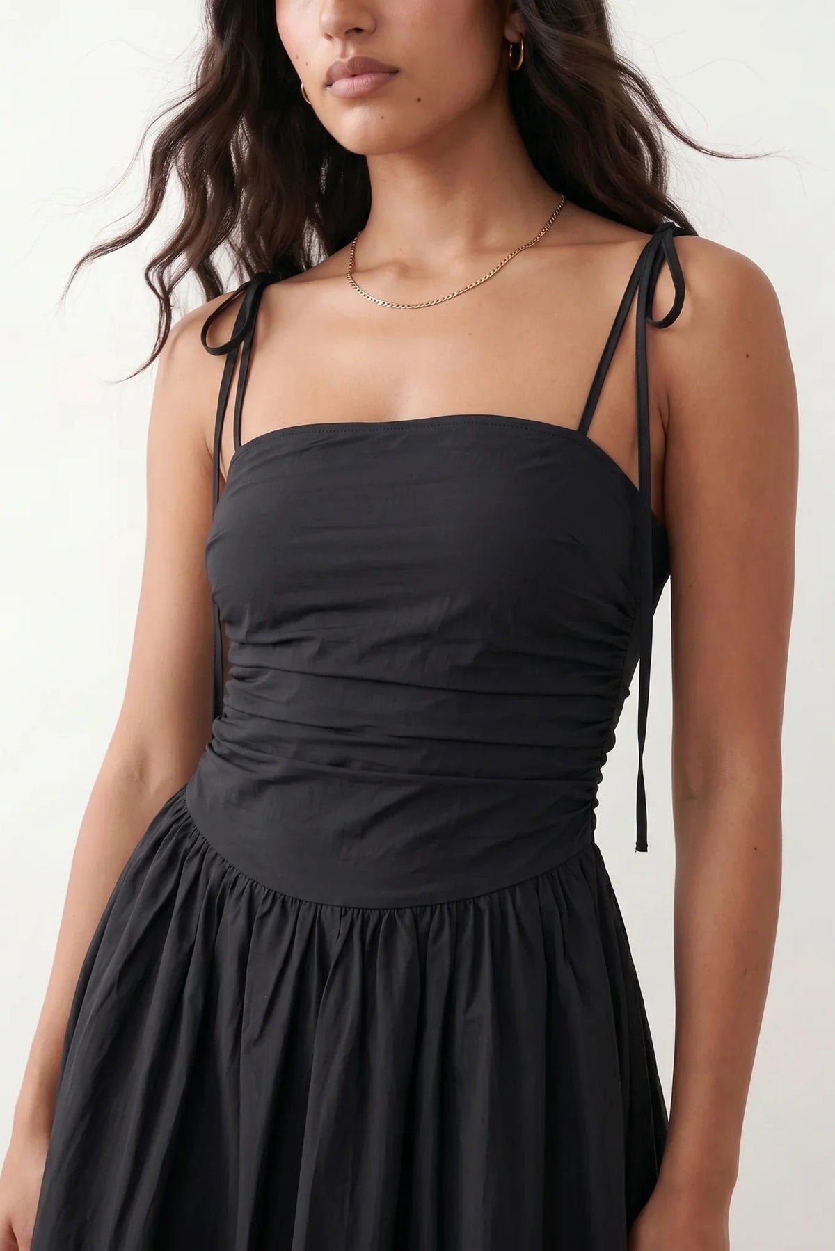 Woman wearing a spaghetti strap low back midi dress with a square neckline, ruched ruffle bodice, adjustable tie shoulder straps, elasticated smocked back, and flowing A-line skirt, styled as an elegant wedding guest and summer occasion dress.