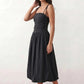 Woman wearing a spaghetti strap low back midi dress with a square neckline, ruched ruffle bodice, adjustable tie shoulder straps, elasticated smocked back, and flowing A-line skirt, styled as an elegant wedding guest and summer occasion dress.
