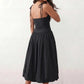Woman wearing a spaghetti strap low back midi dress with a square neckline, ruched ruffle bodice, adjustable tie shoulder straps, elasticated smocked back, and flowing A-line skirt, styled as an elegant wedding guest and summer occasion dress.