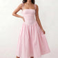 Woman wearing a spaghetti strap low back midi dress with a square neckline, ruched ruffle bodice, adjustable tie shoulder straps, elasticated smocked back, and flowing A-line skirt, styled as an elegant wedding guest and summer occasion dress.