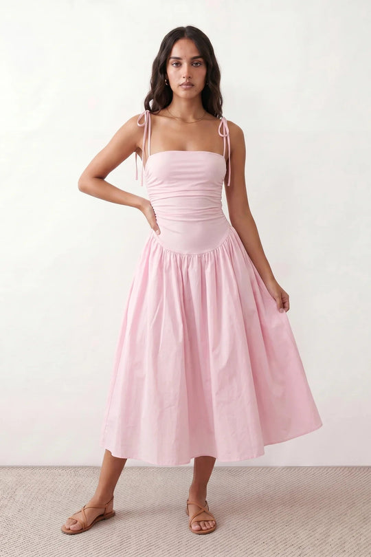Woman wearing a spaghetti strap low back midi dress with a square neckline, ruched ruffle bodice, adjustable tie shoulder straps, elasticated smocked back, and flowing A-line skirt, styled as an elegant wedding guest and summer occasion dress.