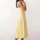 Woman wearing a spaghetti strap low back midi dress with a square neckline, ruched ruffle bodice, adjustable tie shoulder straps, elasticated smocked back, and flowing A-line skirt, styled as an elegant wedding guest and summer occasion dress.
