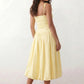 Woman wearing a spaghetti strap low back midi dress with a square neckline, ruched ruffle bodice, adjustable tie shoulder straps, elasticated smocked back, and flowing A-line skirt, styled as an elegant wedding guest and summer occasion dress.
