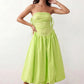 Woman wearing a spaghetti strap low back midi dress with a square neckline, ruched ruffle bodice, adjustable tie shoulder straps, elasticated smocked back, and flowing A-line skirt, styled as an elegant wedding guest and summer occasion dress.