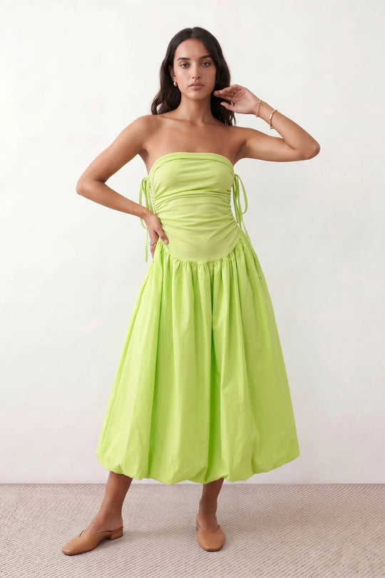 Woman wearing a spaghetti strap low back midi dress with a square neckline, ruched ruffle bodice, adjustable tie shoulder straps, elasticated smocked back, and flowing A-line skirt, styled as an elegant wedding guest and summer occasion dress.
