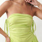 Woman wearing a spaghetti strap low back midi dress with a square neckline, ruched ruffle bodice, adjustable tie shoulder straps, elasticated smocked back, and flowing A-line skirt, styled as an elegant wedding guest and summer occasion dress.