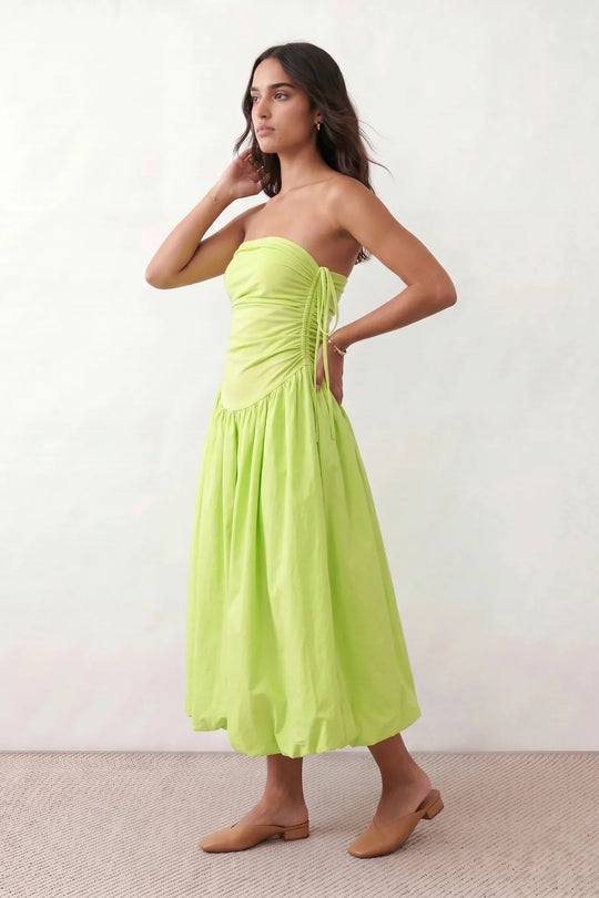 Woman wearing a spaghetti strap low back midi dress with a square neckline, ruched ruffle bodice, adjustable tie shoulder straps, elasticated smocked back, and flowing A-line skirt, styled as an elegant wedding guest and summer occasion dress.