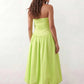 Woman wearing a spaghetti strap low back midi dress with a square neckline, ruched ruffle bodice, adjustable tie shoulder straps, elasticated smocked back, and flowing A-line skirt, styled as an elegant wedding guest and summer occasion dress.