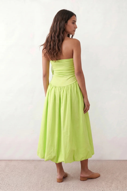Woman wearing a spaghetti strap low back midi dress with a square neckline, ruched ruffle bodice, adjustable tie shoulder straps, elasticated smocked back, and flowing A-line skirt, styled as an elegant wedding guest and summer occasion dress.