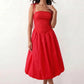 Woman wearing a spaghetti strap low back midi dress with a square neckline, ruched ruffle bodice, adjustable tie shoulder straps, elasticated smocked back, and flowing A-line skirt, styled as an elegant wedding guest and summer occasion dress.