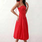Woman wearing a spaghetti strap low back midi dress with a square neckline, ruched ruffle bodice, adjustable tie shoulder straps, elasticated smocked back, and flowing A-line skirt, styled as an elegant wedding guest and summer occasion dress.