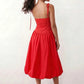 Woman wearing a spaghetti strap low back midi dress with a square neckline, ruched ruffle bodice, adjustable tie shoulder straps, elasticated smocked back, and flowing A-line skirt, styled as an elegant wedding guest and summer occasion dress.