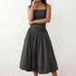 Woman wearing a spaghetti strap low back midi dress with a square neckline, ruched ruffle bodice, adjustable tie shoulder straps, elasticated smocked back, and flowing A-line skirt, styled as an elegant wedding guest and summer occasion dress.