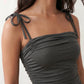 Woman wearing a spaghetti strap low back midi dress with a square neckline, ruched ruffle bodice, adjustable tie shoulder straps, elasticated smocked back, and flowing A-line skirt, styled as an elegant wedding guest and summer occasion dress.