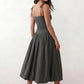 Woman wearing a spaghetti strap low back midi dress with a square neckline, ruched ruffle bodice, adjustable tie shoulder straps, elasticated smocked back, and flowing A-line skirt, styled as an elegant wedding guest and summer occasion dress.