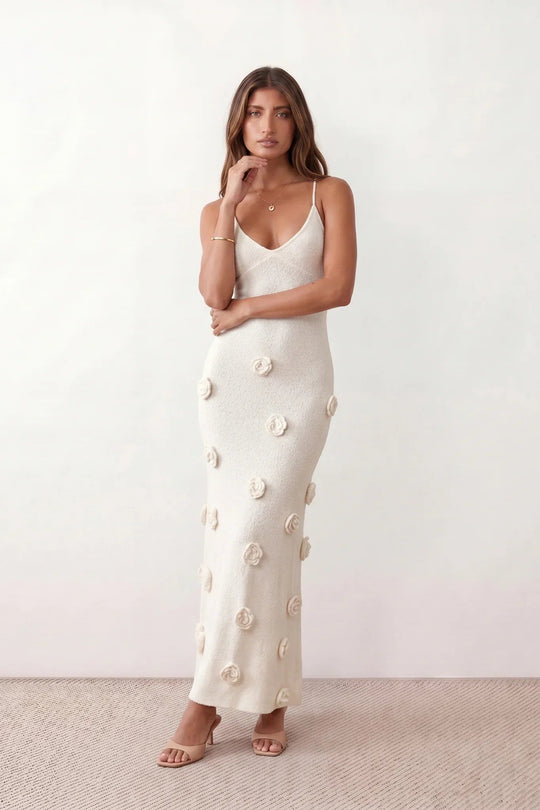 Woman wearing the Spaghetti Strap Open Back Floral Appliqué Maxi Dress featuring a fitted full-length silhouette, elegant V-neckline, adjustable spaghetti straps, delicate 3D floral rosette appliqués, and a lace-up open back, ideal for weddings, black-tie events, and formal occasions.