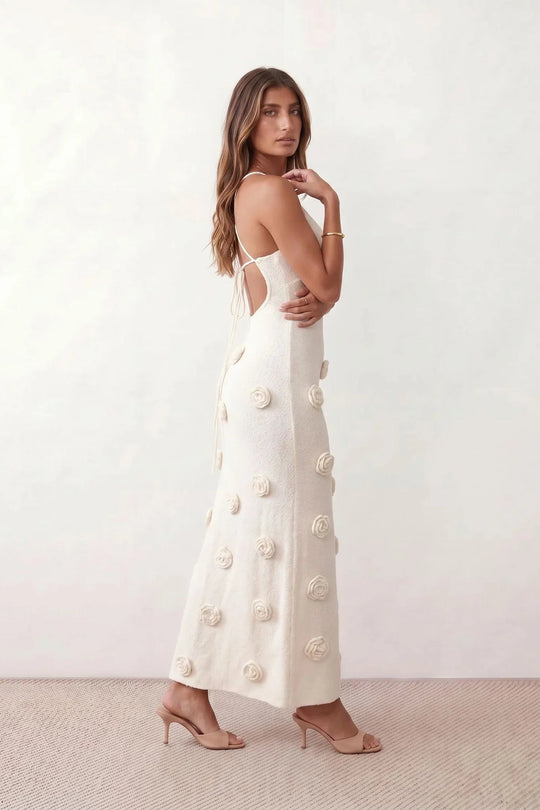 Woman wearing the Spaghetti Strap Open Back Floral Appliqué Maxi Dress featuring a fitted full-length silhouette, elegant V-neckline, adjustable spaghetti straps, delicate 3D floral rosette appliqués, and a lace-up open back, ideal for weddings, black-tie events, and formal occasions.