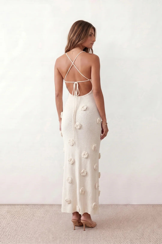 Woman wearing the Spaghetti Strap Open Back Floral Appliqué Maxi Dress featuring a fitted full-length silhouette, elegant V-neckline, adjustable spaghetti straps, delicate 3D floral rosette appliqués, and a lace-up open back, ideal for weddings, black-tie events, and formal occasions.