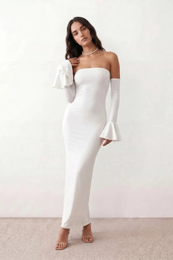 Woman wearing the strapless mermaid maxi dress with a sweetheart neckline, statement shoulder bow, matching long bell-cuff gloves, fitted silhouette and floor-length hem, ideal for weddings, black-tie events and formal occasions.