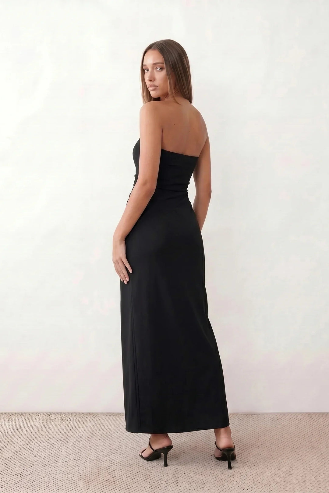 Woman wearing the strapless square neck fitted maxi dress with a structured fold-over bodice, ruched waist, low back and side slit, elegant full-length evening gown for weddings, black-tie events and formal occasions.