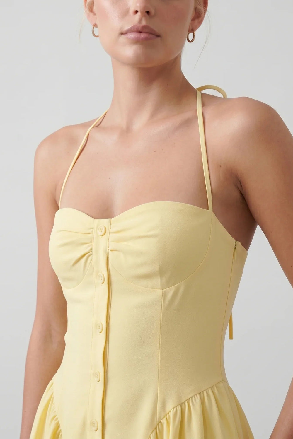 Woman wearing the Sweetheart Halter Neck Corset Mini Dress featuring a ruched sweetheart neckline, structured corset bodice, halter tie neck, open back, decorative button-front detail, and flared mini skirt, styled for weddings, parties, and special occasions.