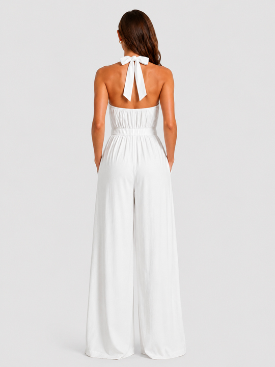 Woman wearing a halter neck wide leg jumpsuit with a defined waistband, flowing silhouette, sleeveless design, and elegant draped fabric for formal occasions.